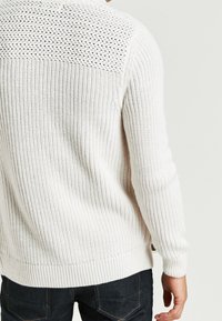 White knit sweater with textured pattern on the back, ribbed cuffs and hem, featuring a relaxed fit and breathable fabric.