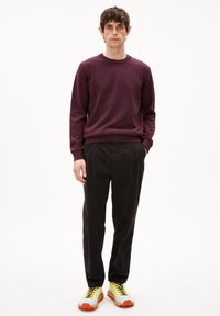 Bordeauxfarbener Sweatshirt, schwarze Hose und gelb-orangefarbene Sneakers. Glatte Textur mit gerippten Bündchen und Saum, sportliches Design, lockere Passform.