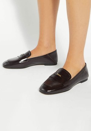 Bruine leren loafers met een puntige neus, voorzien van een debossed band en subtiele gouden hardware accenten. Platte zool voor gemakkelijk dragen.