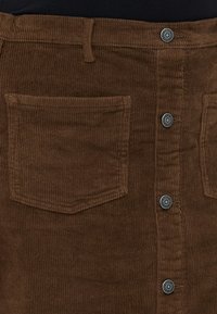 Fustă din corduroy maro, cu un model de nervuri verticale, închidere frontală cu nasturi din metal și două buzunare aplicate la spate.