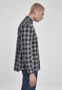 Cămașă din flanel în carouri bleumarin și alb, cu mâneci lungi, guler închis cu nasturi, croială lejeră, vedere laterală, purtată peste blugi albaștri. Țesătură texturată.