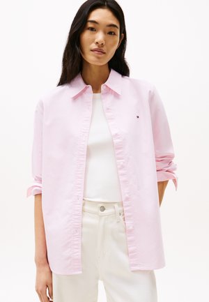 Lichtroze gestreepte blouse met een klassieke kraag, met opgerolde mouwen. Gekozen over een witte top, gecombineerd met lichtgekleurde broek.