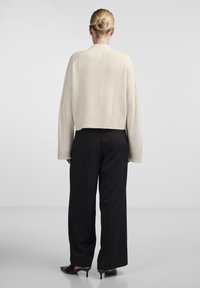 Ανοιχτό μπεζ κοντό πουλόβερ με υφή πλέξης, φαρδιά μανίκια και ριμπ στρίφωμα, συνδυασμένο με ψηλόμεσες μαύρες παντελόνες σε φαρδιά γραμμή και τακούνια.