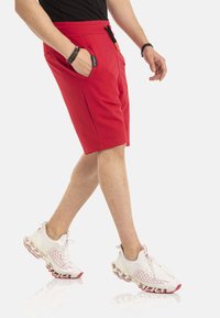 Rode shorts met een elastische tailleband en zijzakken, gecombineerd met witte sportschoenen met een gestructureerde zool en rode accenten.
