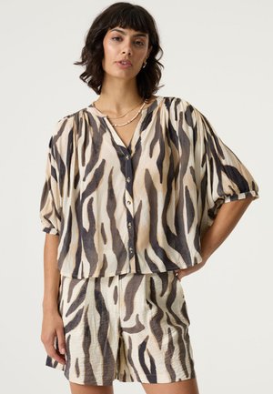 Kurzärmlige, lockere Bluse in Beige mit schwarzem und braunem Animal-Print; mit V-Ausschnitt und Knöpfen. Kombiniert mit passenden Shorts im gleichen Muster.