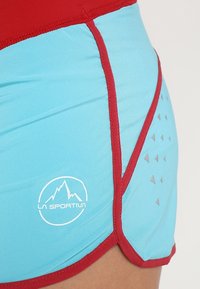 Niebieskie sportowe spodenki z czerwonym pasem i bocznymi szwami, z białym logo i wzorem z małych szarych trójkątów.