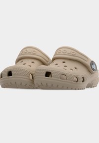 Ζευγάρι μπεζ παπούτσια τύπου κλογκ με τρύπες αερισμού, ρυθμιζόμενα λουράκια στη φτέρνα και υφασμένα πέλματα σε μονόχρωμο φόντο.