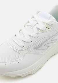 White athletic sneaker featuring a textured leather and mesh upper, round laces, reinforced toe, and a cushioned sole with subtle logo detailing.