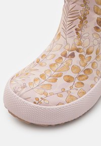 Botte imperméable rose avec un motif de feuilles botaniques en tons dorés et bruns, dotée d'une semelle en caoutchouc blanc texturé et d'une surface lisse.