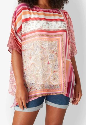 Mujer con una blusa suelta multicolor con estampados florales y geométricos combinada con pantalones cortos de mezclilla remangados.