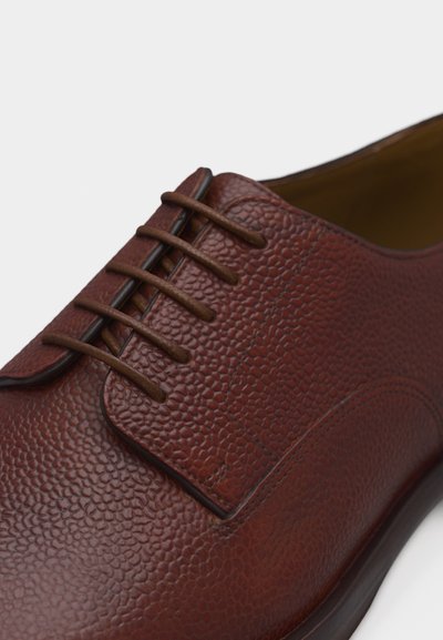 Chaussure habillée en cuir marron avec surface texturée, laçage fermé et semelle marron foncé, vue en gros plan.