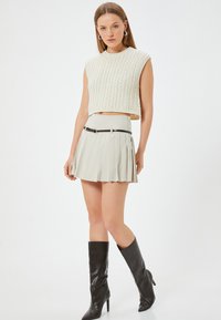 Top corto de punto color crema con patrón texturizado, combinado con una falda mini plisada de color gris claro y botas de cuero negro de tacón alto hasta la rodilla.