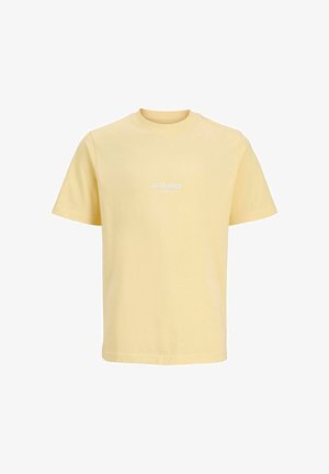 Jachetă din denim albastru închis cu nasturi argintii, purtată peste o cămașă galben deschis. Blugi largi, albastru deschis și adidași albi cu accente albastre.