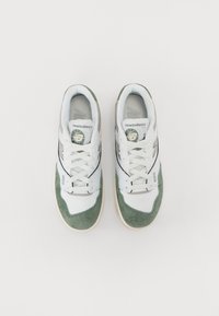Zapatillas blancas y verdes con materiales de malla y ante, con puntera redondeada, cuello acolchado y acentos en negro contrastantes en los lados.