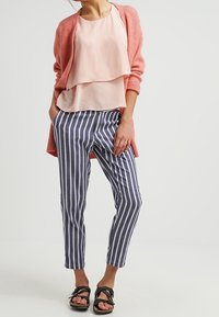 Jasnoróżowa bluzka z warstwami, prążkowany jasnokoralowy kardigan oraz wąskie spodnie w niebieskie paski. Sandały mają czarny design paska.