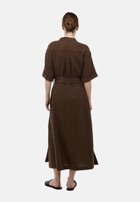Robe maxi marron à côtes avec manches courtes, taille ceinturée et fente dans le dos ; en tissu texturé, elle arrive aux chevilles.