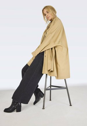 Beige, oversized trench coat made of lightweight material, paired with high-waisted, dark denim jeans and black heeled ankle boots.