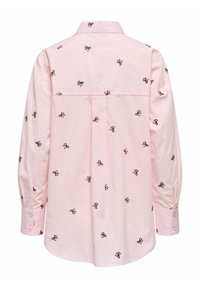 Oblečena svetlo roza srajca z dolgimi rokavi, širokim ovratnikom, zapenjanimi manšetami in majhnimi temno rjavimi vezenimi vzorci lokov, razpršenimi po tkanini.