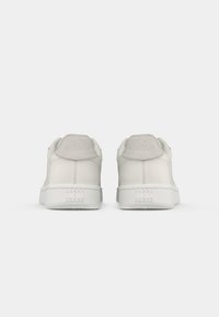 Adidași din piele albă cu accente texturate din suede gri, talpă din cauciuc albă plată și detaliu de marcă pe călcâi. Design simplu și minimalist.