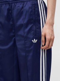 Μπλε σκούρο παντελόνι φόρμας Adidas με λευκές τρεις ρίγες στο πλάι και τσέπη με φερμουάρ κοντά στη μέση με το λογότυπο Adidas trefoil.
