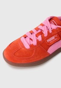 Puma Palermo tossut kirkkaan oranssista mokasta, joissa on vaaleanpunaiset nauhat ja yksityiskohdat. Varustettu kumipohjalla ja ommelluilla yksityiskohdilla.