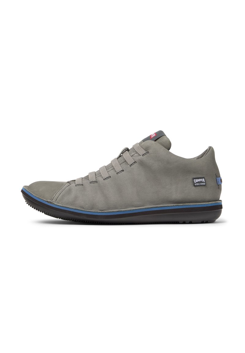 Scarpa casual grigia con punta curva, lacci elastici e suola blu a contrasto. Presenta un logo sul lato esterno.