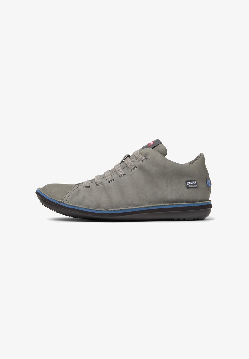 Scarpa casual grigia con punta curva, lacci elastici e suola blu a contrasto. Presenta un logo sul lato esterno.