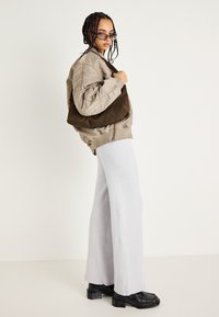 Bolsa de ombro em camurça castanha, jaqueta bomber bege oversized, calças largas cinza claro, sapatos chunky pretos, cabelo trançado e óculos de sol.