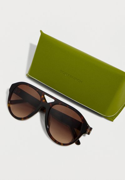 Γυαλιά ηλίου με σκελετό χελώνας και φακούς καφέ με βαθμιαία απόχρωση τοποθετημένα δίπλα σε θήκη γυαλιών ηλίου lime πράσινου χρώματος Tory Burch πάνω σε λευκή επιφάνεια.