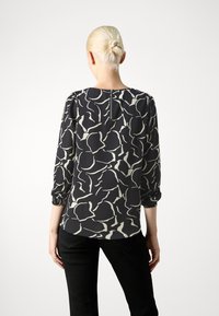 Blusa nera con un leggero motivo astratto, maniche lunghe con polsini elastici e chiusura con cerniera sul retro. Tessuto morbido con una leggera lucentezza.