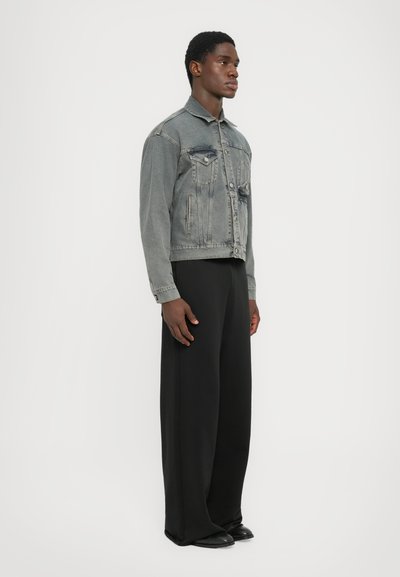 Jachetă din denim în gri estompat, cu un design structurat, buzunare frontale și închidere cu butoane, asortată cu pantaloni largi negri și pantofi negri.