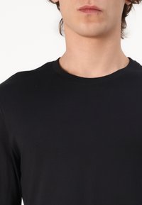 Sort langærmet t-shirt med rund halsudskæring, lavet af blødt bomuldsstof. Har en glat tekstur og en tætsiddende pasform.