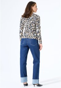 Langärmliges Oberteil mit Leopardenmuster in Beige und Schwarz, kombiniert mit hoch taillierten blauen Jeans mit umgeschlagenen Säumen und geradem Schnitt.