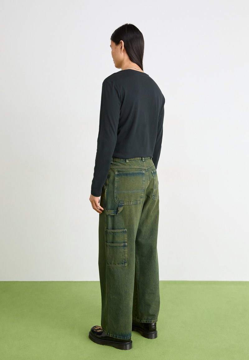 Top nero a maniche lunghe abbinato a pantaloni cargo verdi oversize con molte tasche e cuciture a vista, indossato con scarpe nere chunky.
