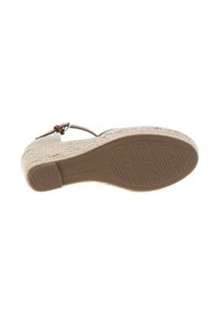 Semelle en beige tissée avec texture tressée, bride de cheville réglable en marron, semelle moulée avec grip texturé et marquage de la marque en dessous.