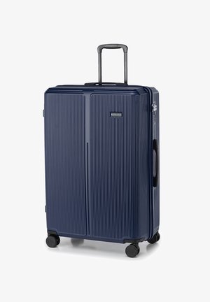 Navy hardshell suitcase with vertical ridges, telescopic handle, top and side carry grips, and four black wheels for mobility.