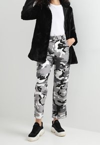 Sort faux fur frakke over en hvid top, parret med grå camouflage cargo bukser og sorte sneakers med hvide såler.
