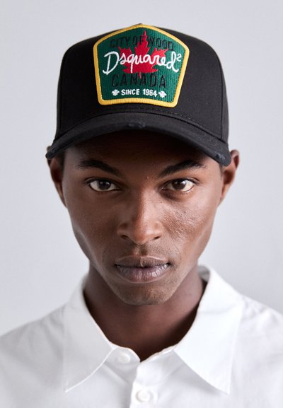 Schwarze Baseballmütze mit einem grünen und goldenen Patch, auf dem "CITY OF WOOD" und "Dsquared² CANADA seit 1964" steht, akzentuiert von roten Ahornblättern.