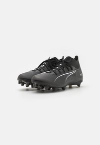 Ghete de fotbal negre cu un superior texturat, logo alb și sireturi; include țepi conici pe talpa exterioară pentru tracțiune.