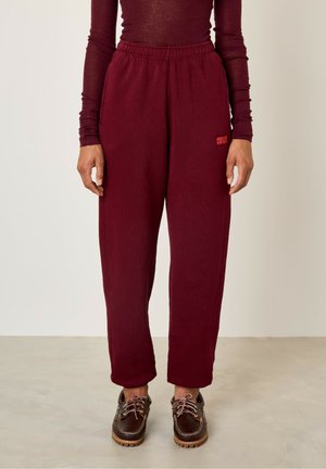 Burgundy sweatpants with an elastic waistband, loose fit, and subtle texture. Features a small "American Vintage" logo on the side.