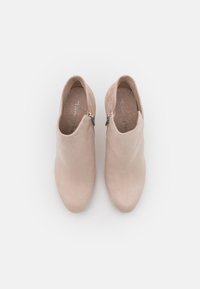 Un par de botas de tobillo de ante beige con cremalleras laterales, vistas desde arriba sobre un fondo blanco liso.