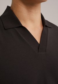 Čierny polo tričko s výstrihom do V a krátkym golierom. Hladká textúra s jemným leskom; má prešitý výstrih a čistý, minimalistický dizajn.