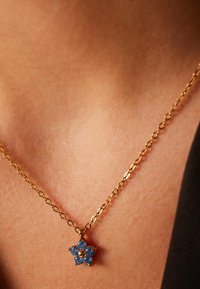 Gouden ketting met een blauwe, bloemvormige hanger met zes bloemblaadjes, elk versierd met een blauwe steen en een centrale gouden kraal.