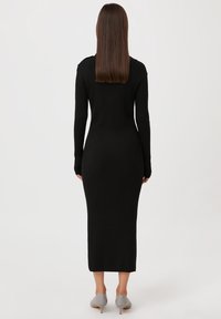 Robe midi noire à côtes avec manches longues, silhouette ajustée et décolleté rond, assortie à des chaussures à talons gris clair.