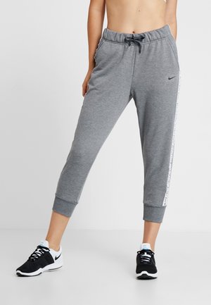 Person wearing grey cropped sweatpants with side stripe and black-and-white Nike sneakers, standing against a plain background.