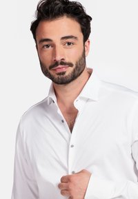 Witte katoenen shirt met een puntige kraag en knoopsluiting aan de voorkant. Heeft een gladde textuur en grijze knopen, met een getailleerde pasvorm.