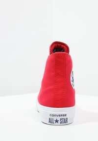 Sneaker alta in tela rossa con logo rotondo sul lato, suola in gomma bianca e dettagli di cucitura lungo il retro.