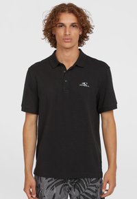 Sort polo shirt i tekstureret stof med en tre-knaps stolpe og et lille hvidt logo på venstre bryst. Korte ærmer.