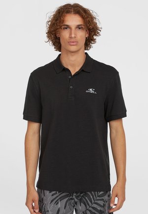 Sort polo shirt i tekstureret stof med en tre-knaps stolpe og et lille hvidt logo på venstre bryst. Korte ærmer.