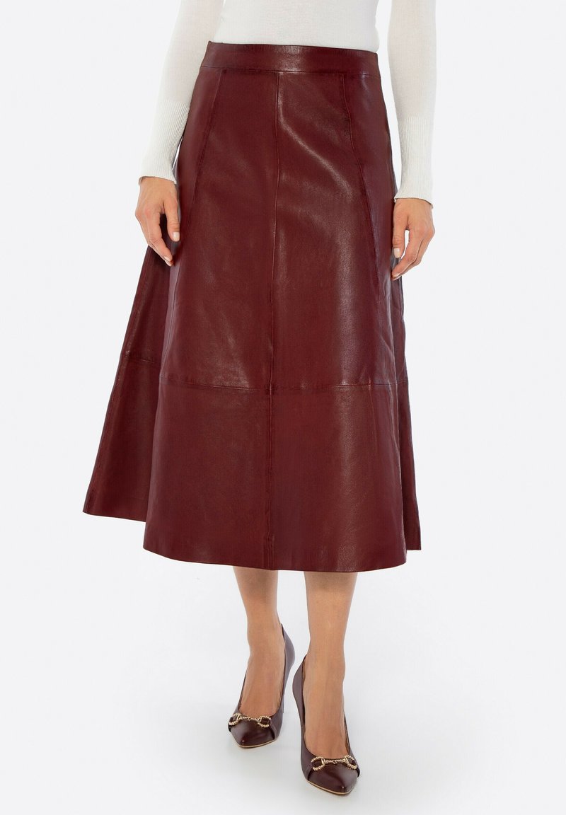 Bordeauxrode leren A-lijn rok met een hoge taille, een gladde textuur en zichtbare stiknaden. Gecombineerd met donkere hakken met metalen accenten.